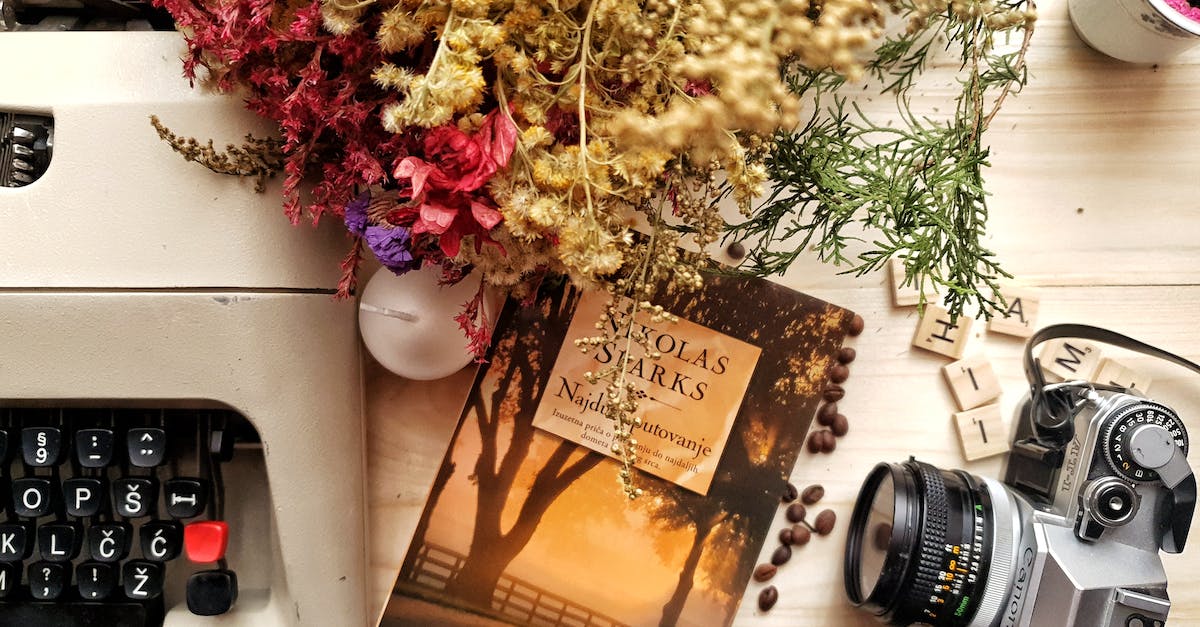 Bunch of flowers and book arranged on wooden table with vintage typewriter and camera