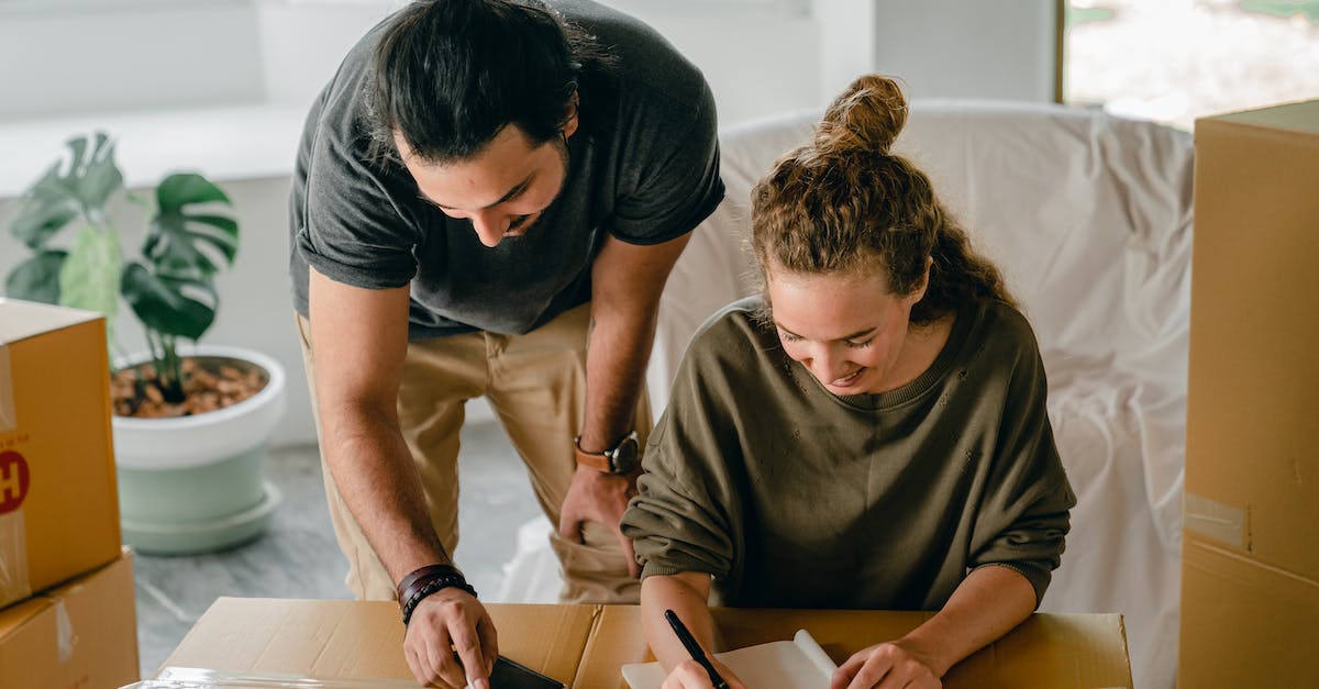 Cheerful diverse couple writing in notebook near boxes before relocation